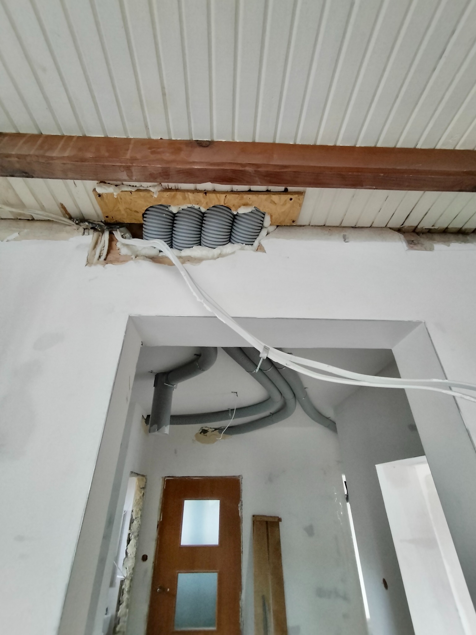 Montaż instalacji wentylacyjnej: widok na szare rury wentylacyjne zamontowane pod sufitem z białych paneli, z widocznym fragmentem drewnianej belki i izolacją piankową, oraz fragmentem instalacji...