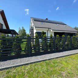 PRO-SPAW Bartosz Białas - Nowoczesna, grafitowa brama wjazdowa z poziomymi zdobieniami, otoczona żywopłotem, na tle domu z panelami słonecznymi i błękitnym niebem.