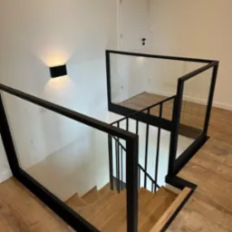 Nowoczesne schody z drewnianymi stopniami i balustradami szklanymi w czarnej ramie w Lubcz Wielki. Minimalistyczny design, widok z góry.