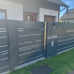 PRO-SPAW Bartosz Białas - Nowoczesna, szara brama wjazdowa z poziomymi szczeblami, numerem domu 'Liliowa 9' i wideodomofonem, na tle domu z drewnianymi elementami.