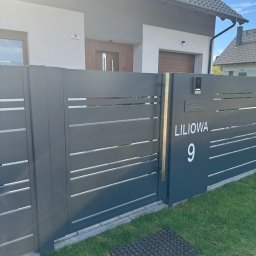 PRO-SPAW Bartosz Białas - Nowoczesna brama wjazdowa w kolorze antracytowym z poziomymi panelami i numerem domu 'Liliowa 9', na tle jasnego domu z drewnianymi akcentami.