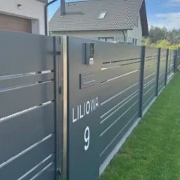 Nowoczesne, antracytowe ogrodzenie panelowe z adresem 'Liliowa 9', skrzynką pocztową i domofonem na tle zielonego trawnika i zabudowy jednorodzinnej.