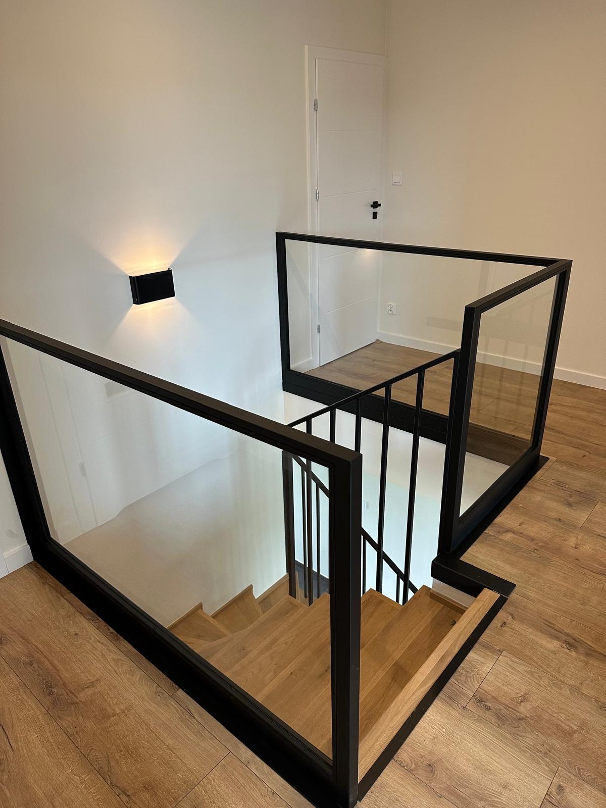 Nowoczesne schody z drewnianymi stopniami i balustradami szklanymi w czarnej ramie w Lubcz Wielki. Minimalistyczny design, widok z góry.