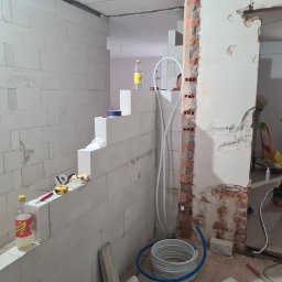 VADYM NIKOLAIEV UBR - Wnętrze w trakcie remontu: ściana z białych bloczków, instalacja wodna, fragment ściany z cegły. Widoczne narzędzia i materiały budowlane. Prace murarskie i instalacyjne w toku.