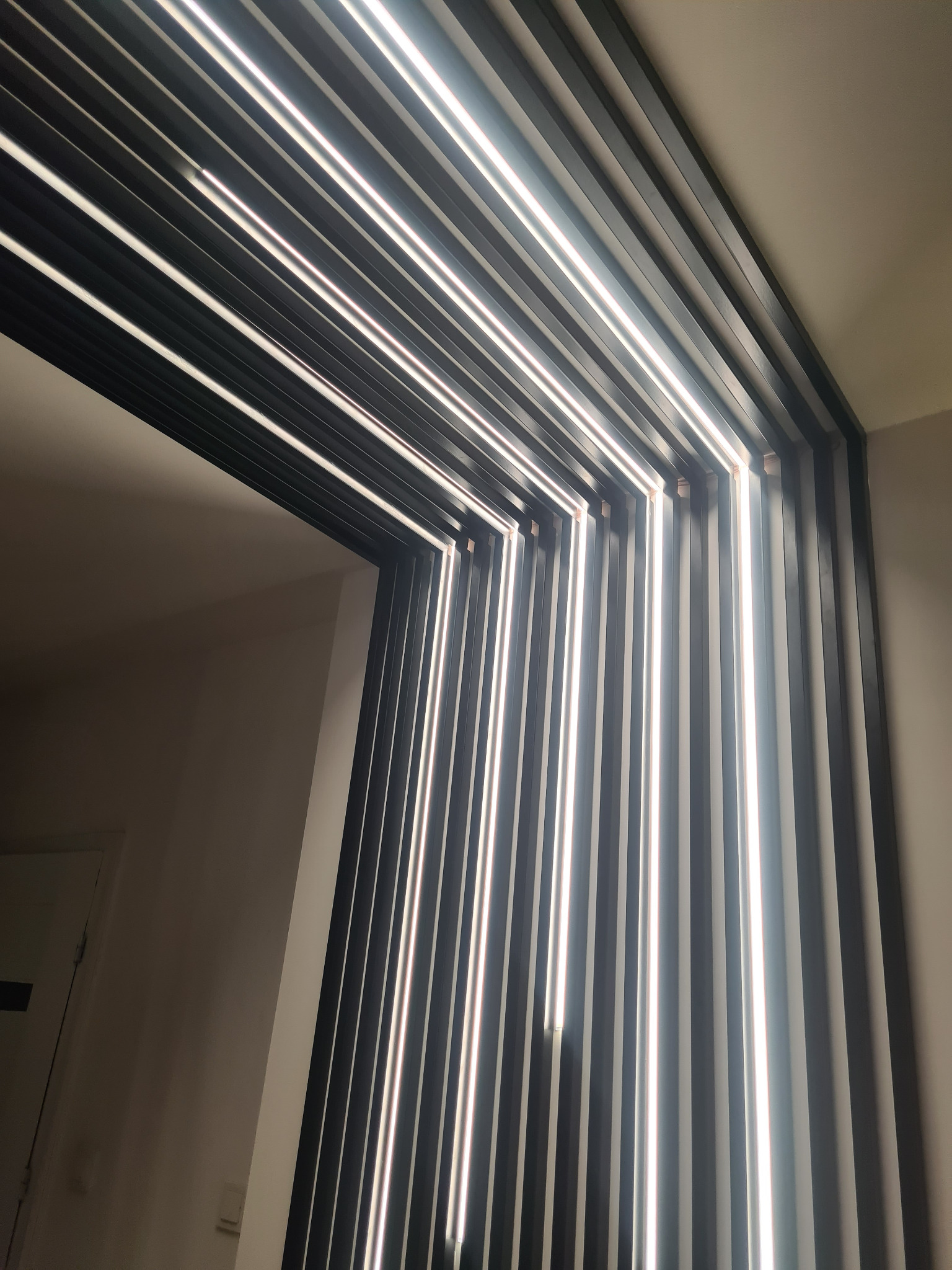 Nowoczesna konstrukcja z czarnych listew i białego oświetlenia LED tworząca geometryczny wzór na suficie, widoczna z perspektywy wejścia do pomieszczenia.