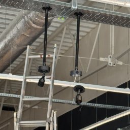 PROTOM SPÓŁKA Z OGRANICZONĄ ODPOWIEDZIALNOŚCIĄ - Dwa czarne reflektory przemysłowe zamontowane pod sufitem, widoczne kable i metalowa drabina.