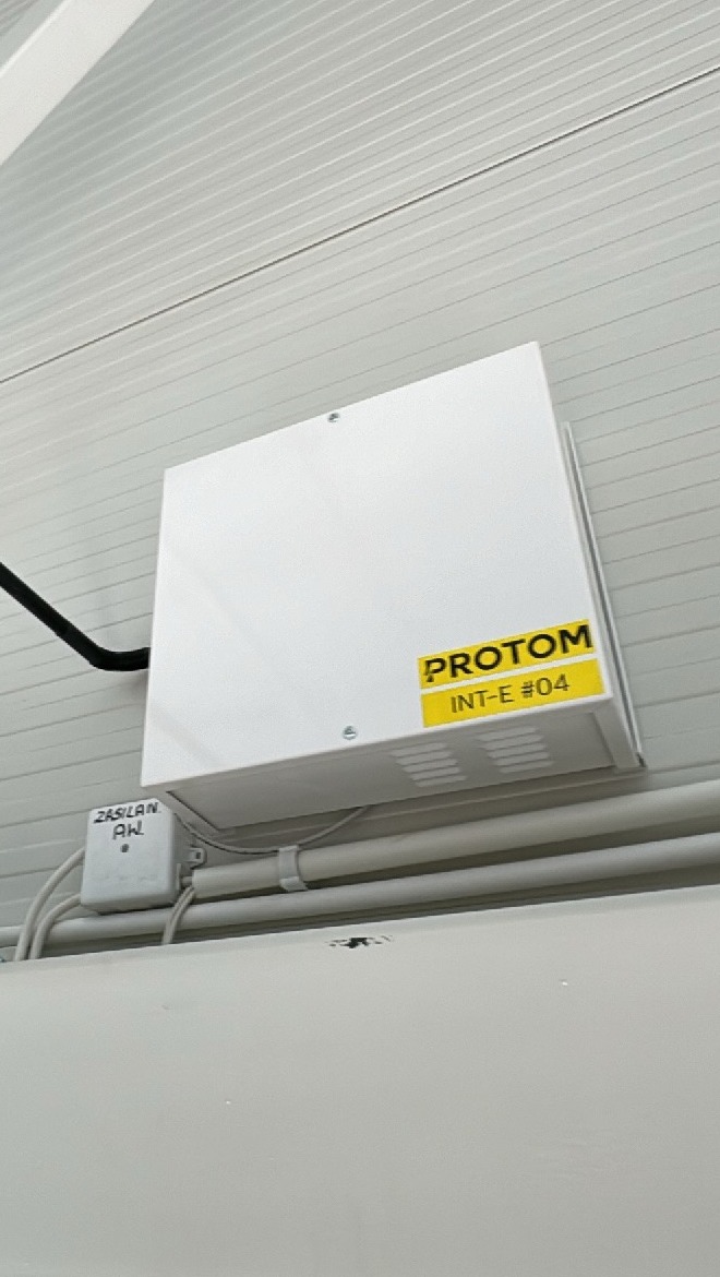 Biała skrzynka z napisem PROTOM INT-E #04, zamontowana na ścianie w Krakowie, z widocznym okablowaniem i elementami instalacji elektrycznej.