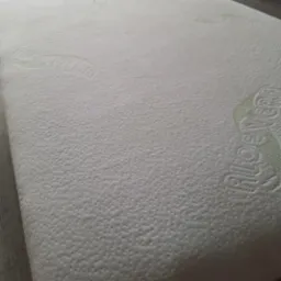 Jasny materac z tłoczonym wzorem i logo 'Aloe Vera', leżący na podłodze z paneli.