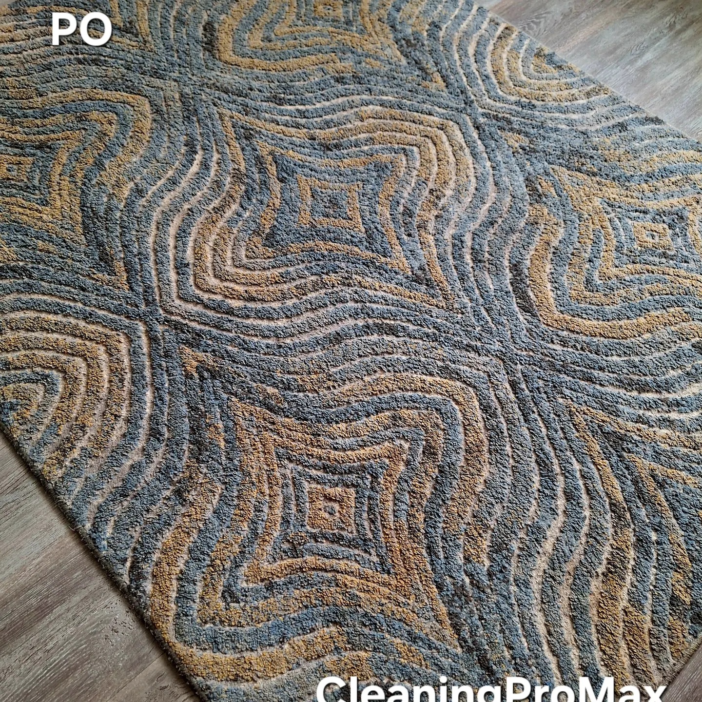 Wzorzysty dywan z efektem 3D w odcieniach szarości i złota, leżący na panelach podłogowych, z widocznym logo firmy w rogu.