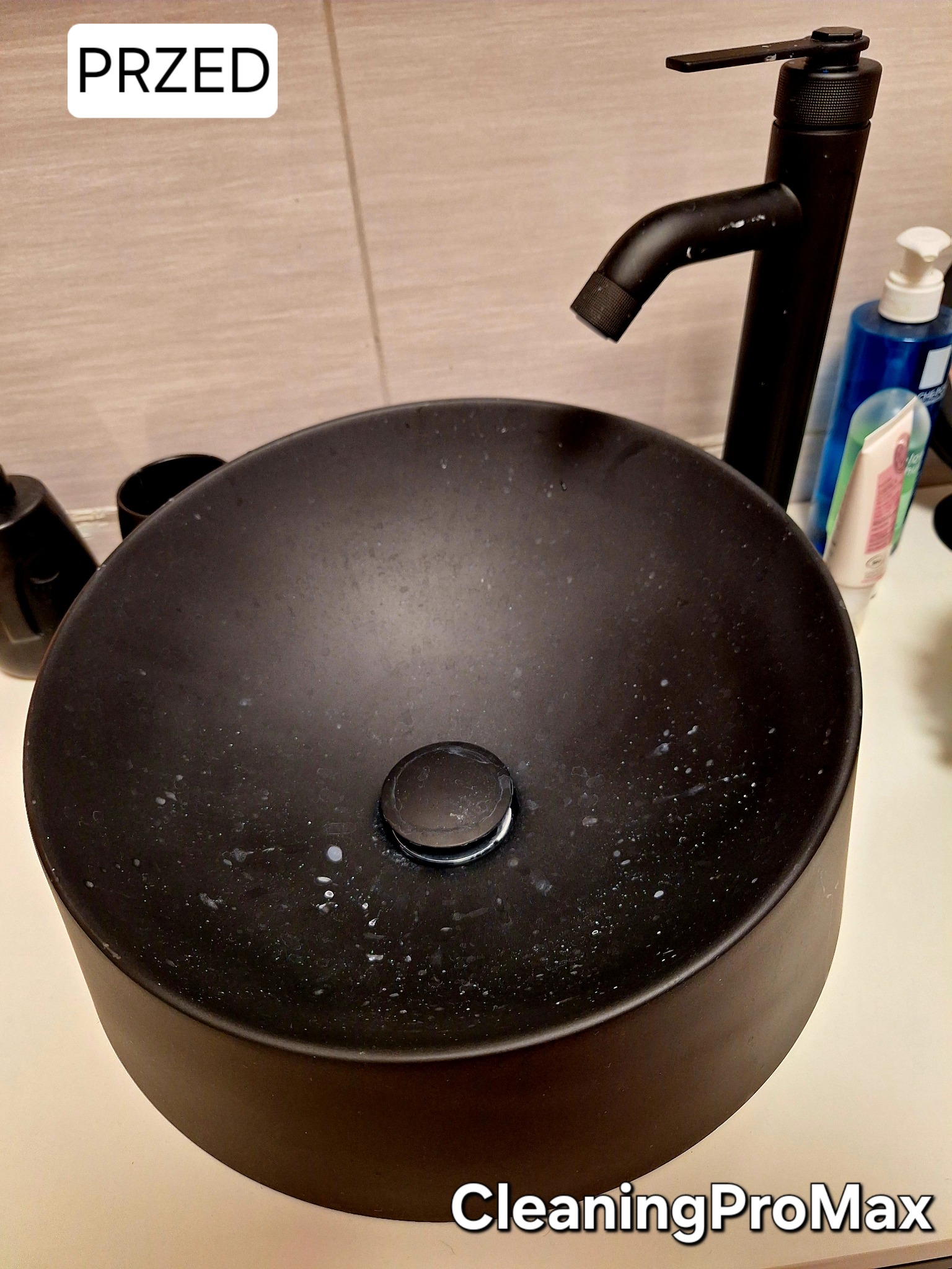 Czarna, okrągła umywalka nablatowa, pokryta zaschniętymi plamami, z czarną armaturą w tle, stan 'przed' czyszczeniem.