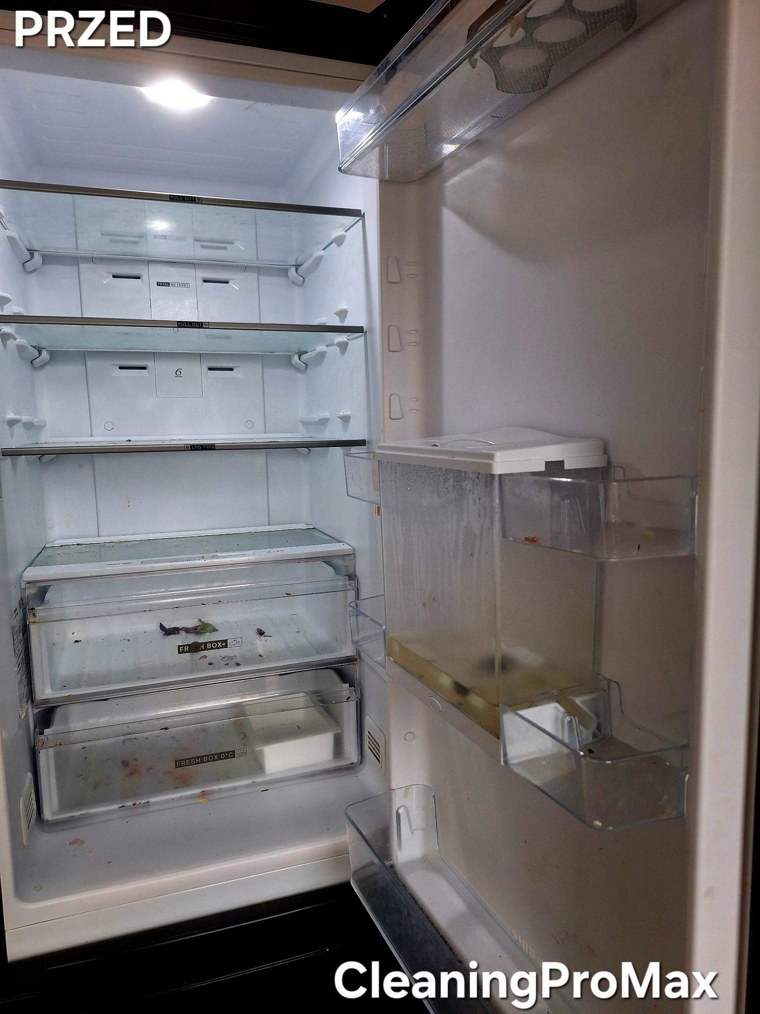Wnętrze brudnej lodówki przed sprzątaniem, widoczne resztki jedzenia na półkach i w szufladach, osad na ściankach, oświetlenie wewnętrzne włączone.