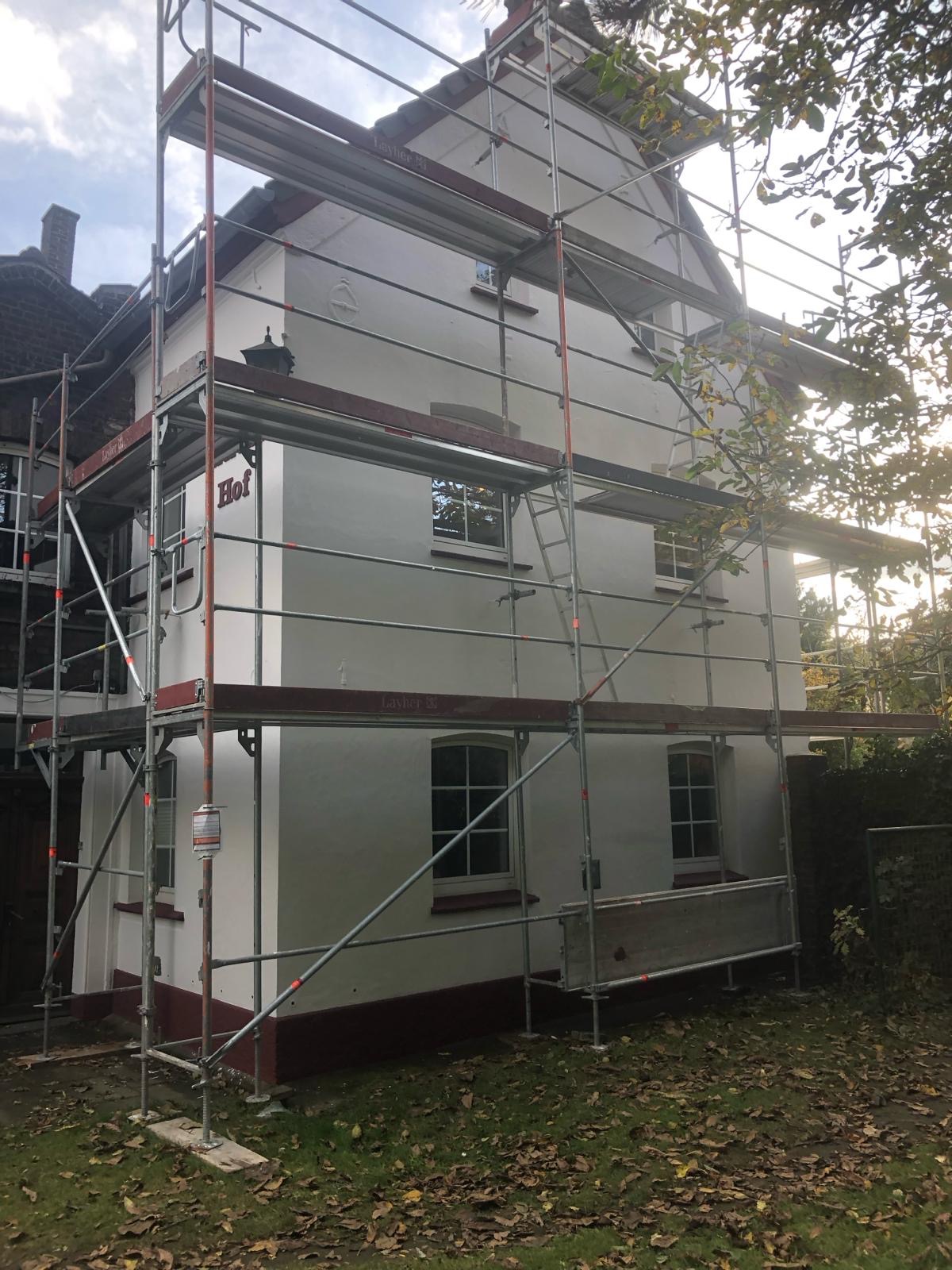 Dwupiętrowy budynek w trakcie prac elewacyjnych, otoczony rusztowaniem, z widocznym napisem 'Hof' na ścianie.