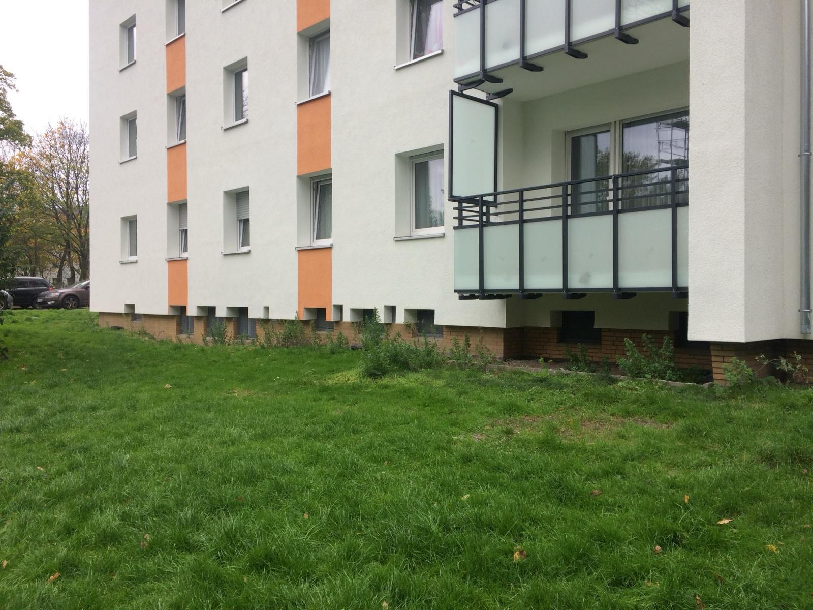 Fragment odnowionego bloku mieszkalnego z balkonem, pomalowanego na biało z pomarańczowymi akcentami, widok z poziomu trawnika.