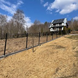 Łukasz Szlembarski - Nowoczesne ogrodzenie panelowe w kolorze czarnym, z betonową podmurówką, otaczające posesję z domem z panelami słonecznymi w tle, na przygotowanym terenie.