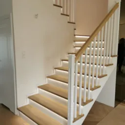 Nowoczesne schody drewniane z białymi balustradami i subtelnym oświetleniem LED pod stopniami, widok z dołu.