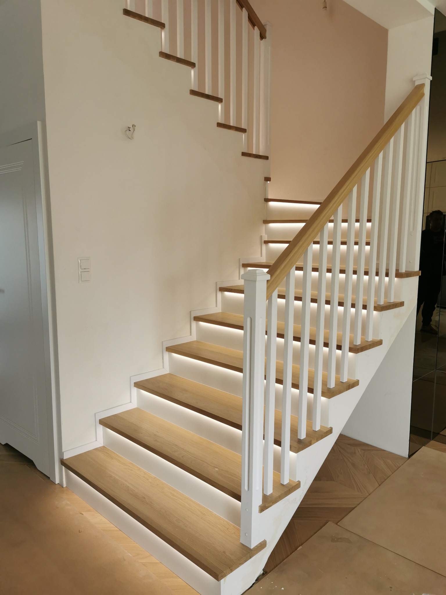 Nowoczesne schody drewniane z białymi balustradami i subtelnym oświetleniem LED pod stopniami, widok z dołu.