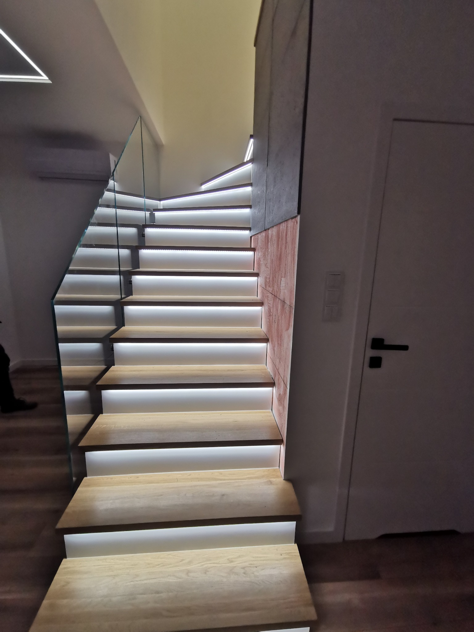 Nowoczesne schody z podświetlanymi stopniami i szklaną balustradą, widok z dołu.