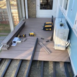 Clover - Montaż desek na balkonie: widoczne legary, częściowo ułożone deski, narzędzia i klimatyzator przy ścianie.