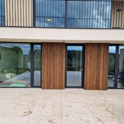 Clover - Nowoczesny taras z płyt kamiennych z przesuwnymi panelami drewnianymi i widokiem na ogród przez szklane drzwi.