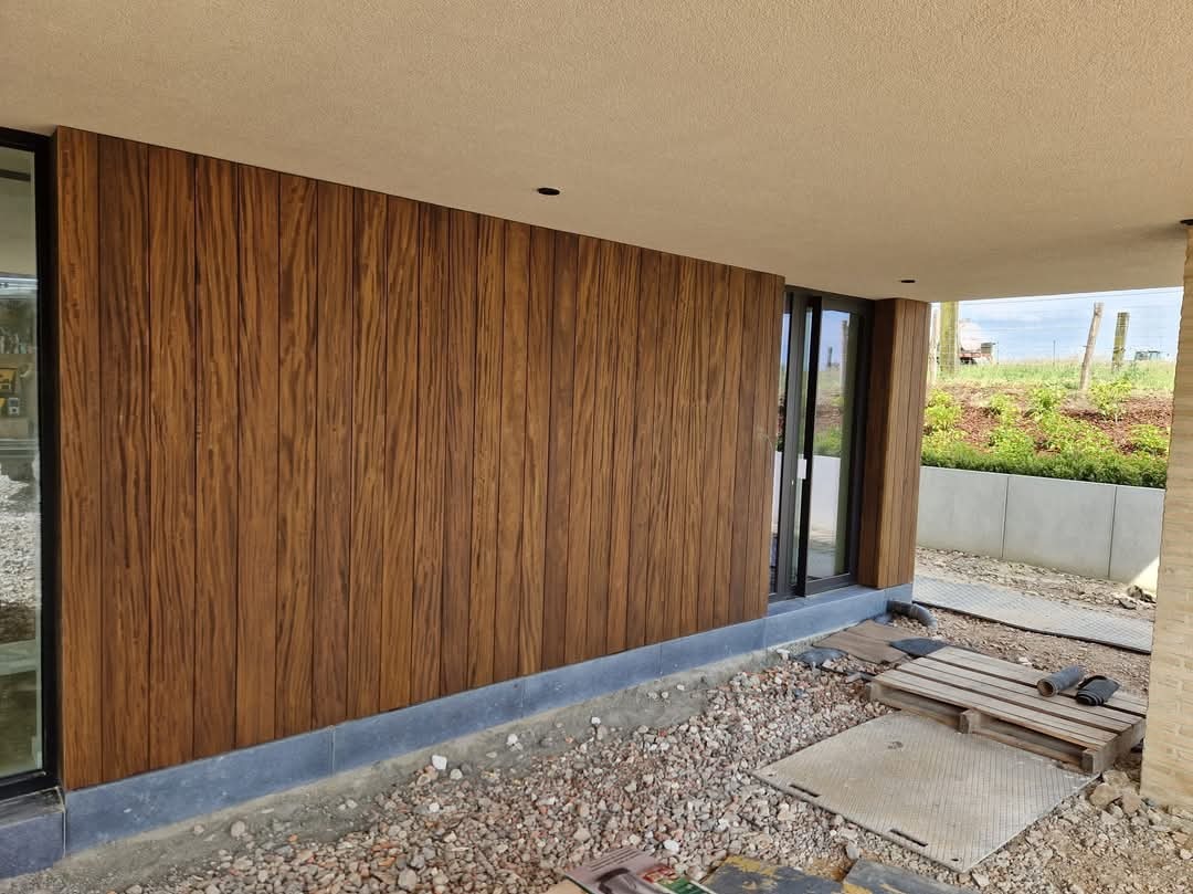 Fragment elewacji budynku wykończony panelami imitującymi drewno z widocznym detalami montażu oraz otoczeniem placu budowy.