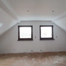 Poddasze ze skośnymi ścianami i dwoma oknami dachowymi, dodatkowo dwa okna na ścianie szczytowej, ściany pomalowane na biało, podłoga z płyt OSB przed położeniem podłogi.