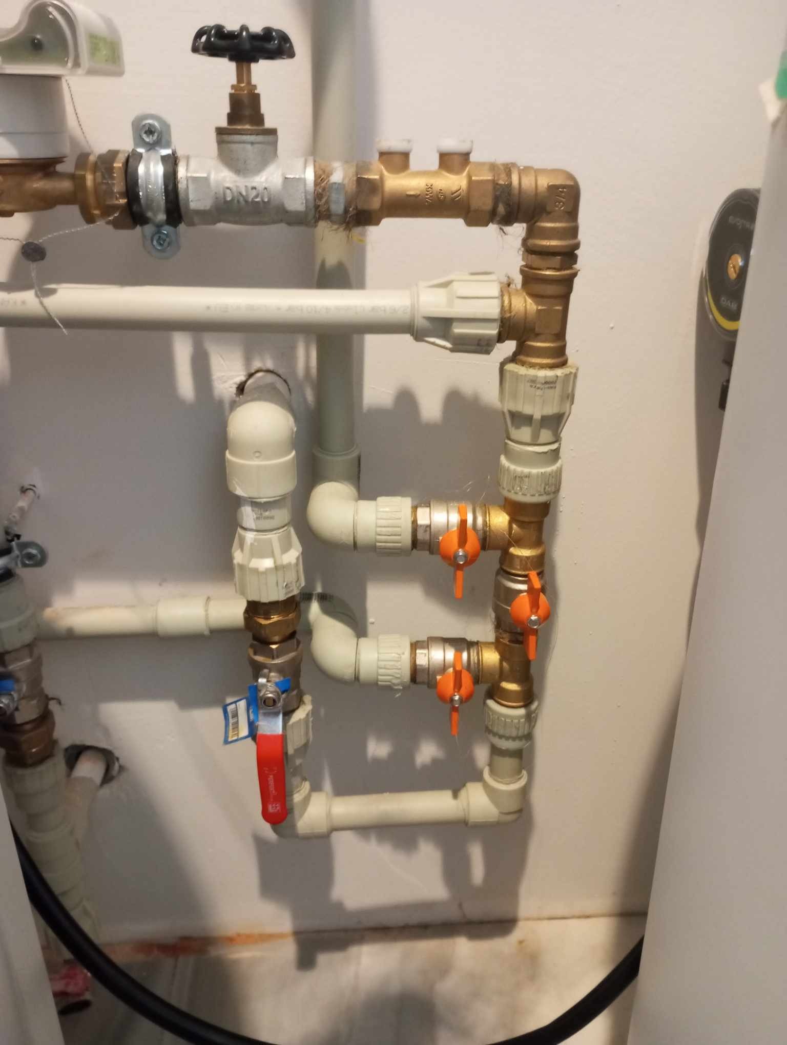 Złożony układ rur z zaworami i złączkami z tworzywa i mosiądzu na tle białej ściany, widoczne ślady po instalacji.