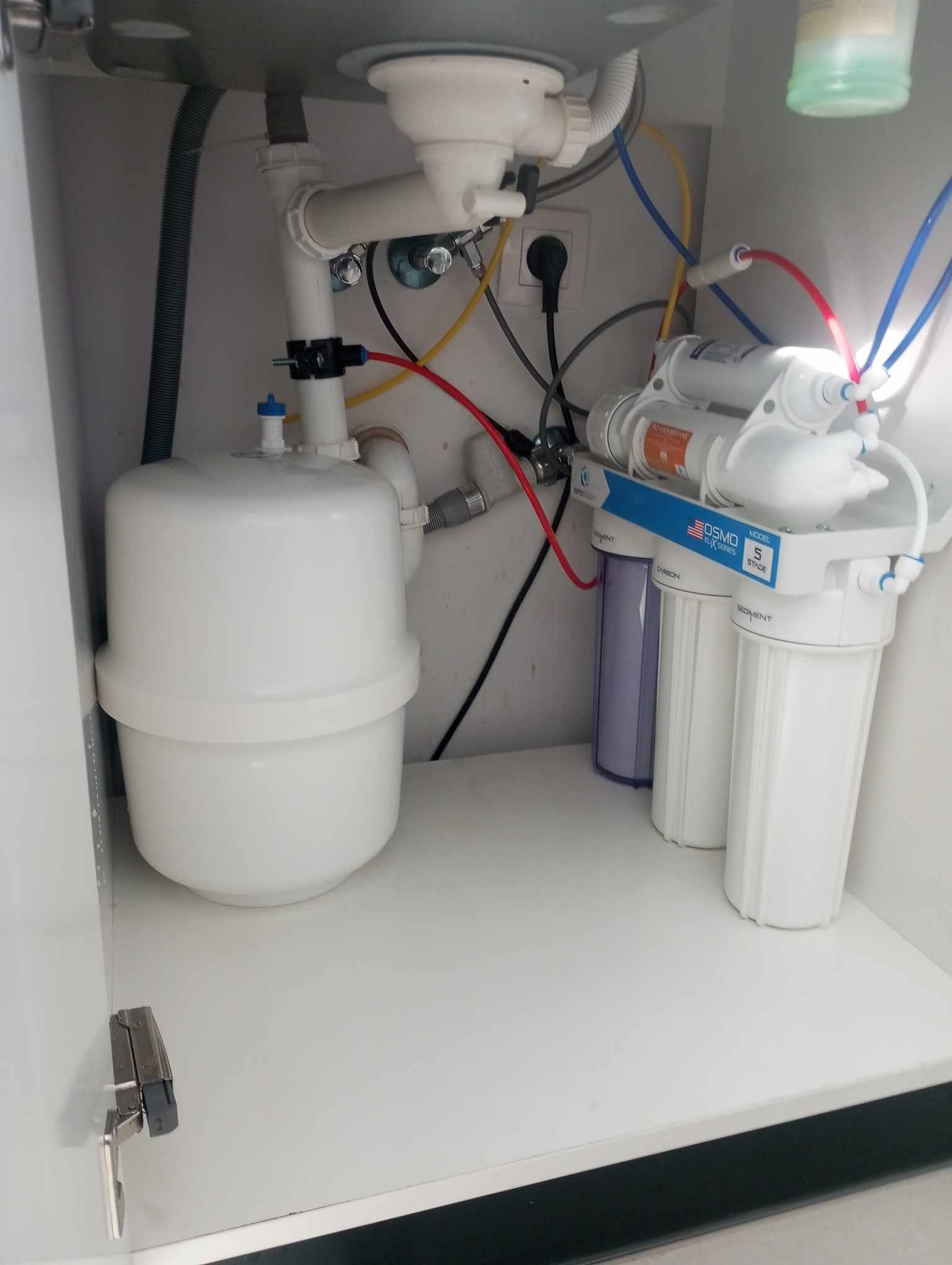 System filtracji wody RO5 zainstalowany pod zlewem, widoczne białe filtry i zbiornik ciśnieniowy, kolorowe wężyki i podłączenie do kanalizacji.