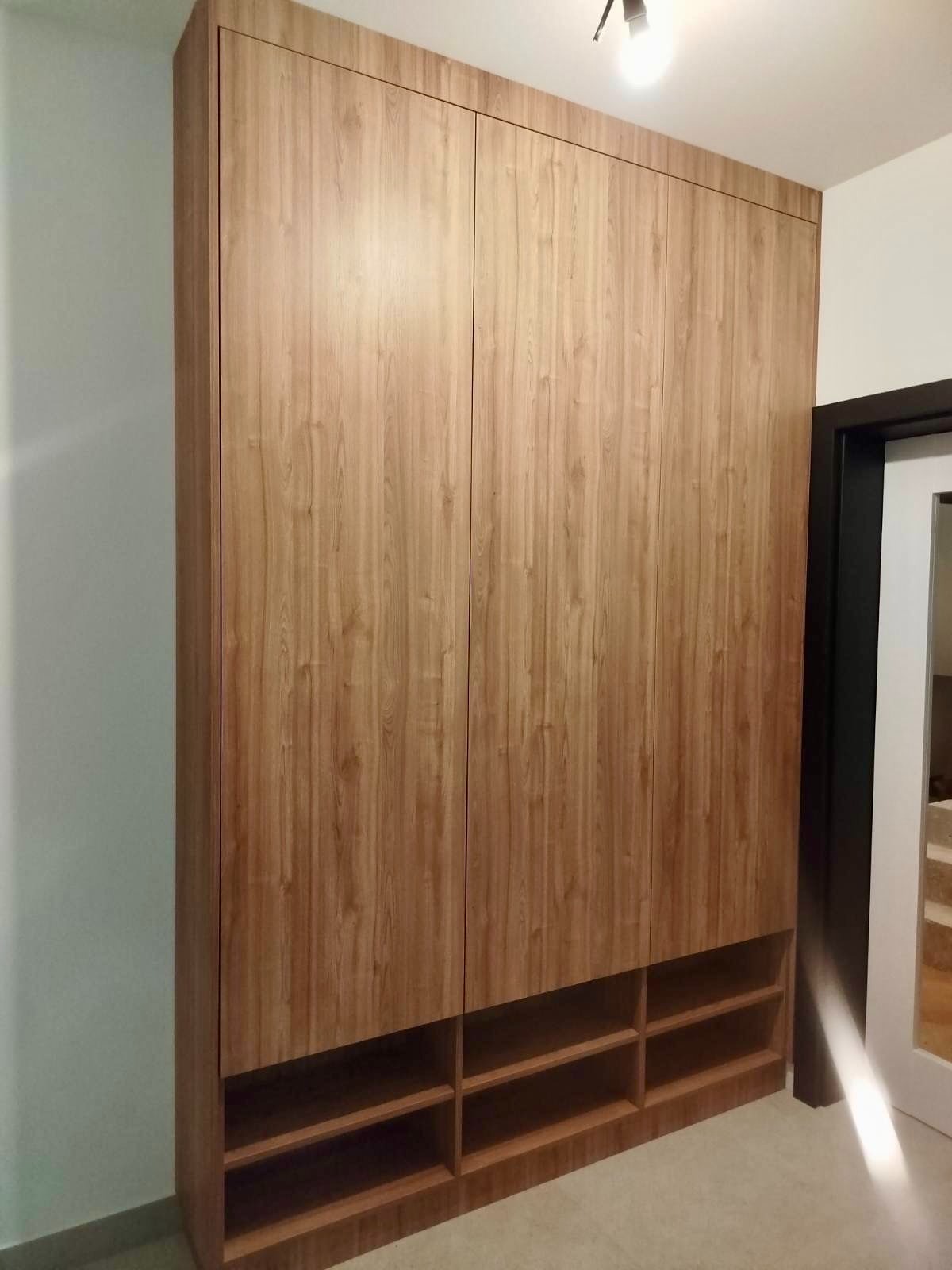 Wysoka szafa wnękowa z drewnopodobnymi frontami i otwartymi półkami u dołu, dopasowana do sufitu, z czarną ościeżnicą drzwi w tle.