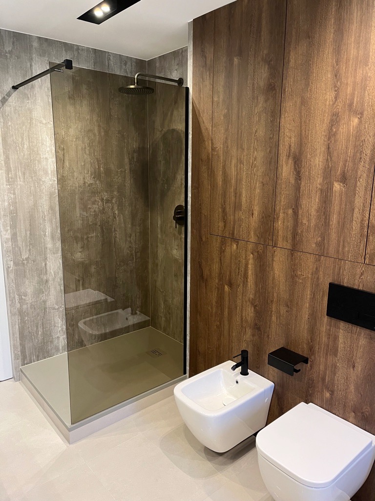 Nowoczesna łazienka z kabiną prysznicową typu walk-in, wykończona płytkami imitującymi beton i drewnem, z czarną armaturą i minimalistyczną toaletą oraz bidetem.
