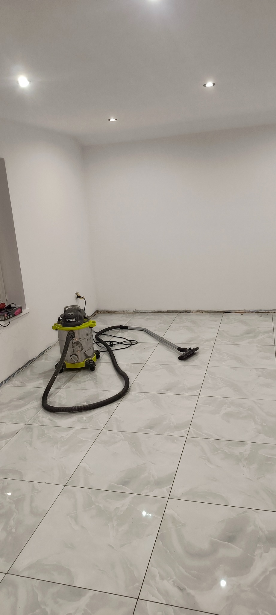 Świeżo ułożone, jasne płytki podłogowe z marmurkowym wzorem, czyszczone przemysłowym odkurzaczem Ryobi po zakończeniu prac.