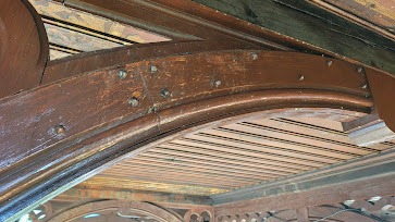 Drewniana konstrukcja z widocznymi śladami zabrudzeń i patyny, ukazana z perspektywy żabiej, podkreślająca detale i fakturę materiału. Widoczne elementy dekoracyjne.