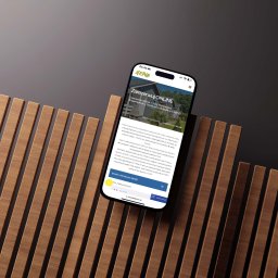 SOCIALBUZZSTUDIO Sp. z o.o. - Smartfon prezentuje stronę internetową z możliwością rezerwacji domków letniskowych NEMO, umieszczony na tle z drewnianych listew.