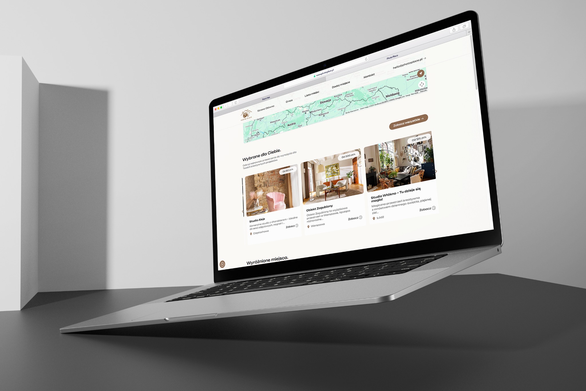 Laptop z otwartą stroną internetową Photo Place, prezentującą mapę i oferty wynajmu przestrzeni kreatywnych. Minimalistyczne tło, nowoczesny design.