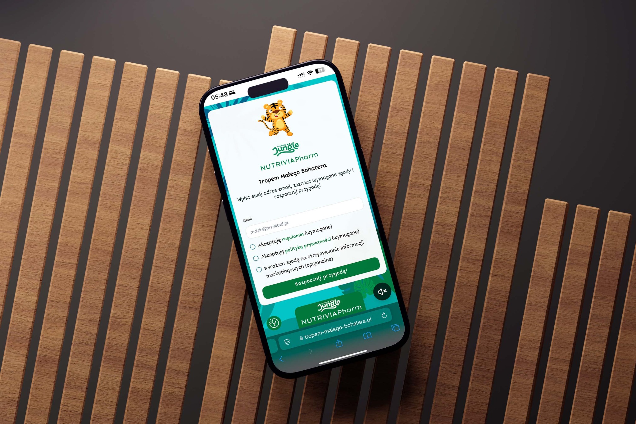 Ekran smartfona prezentuje formularz rejestracyjny na stronie internetowej z motywem dżungli, na tle drewnianej ściany z pionowych listew.