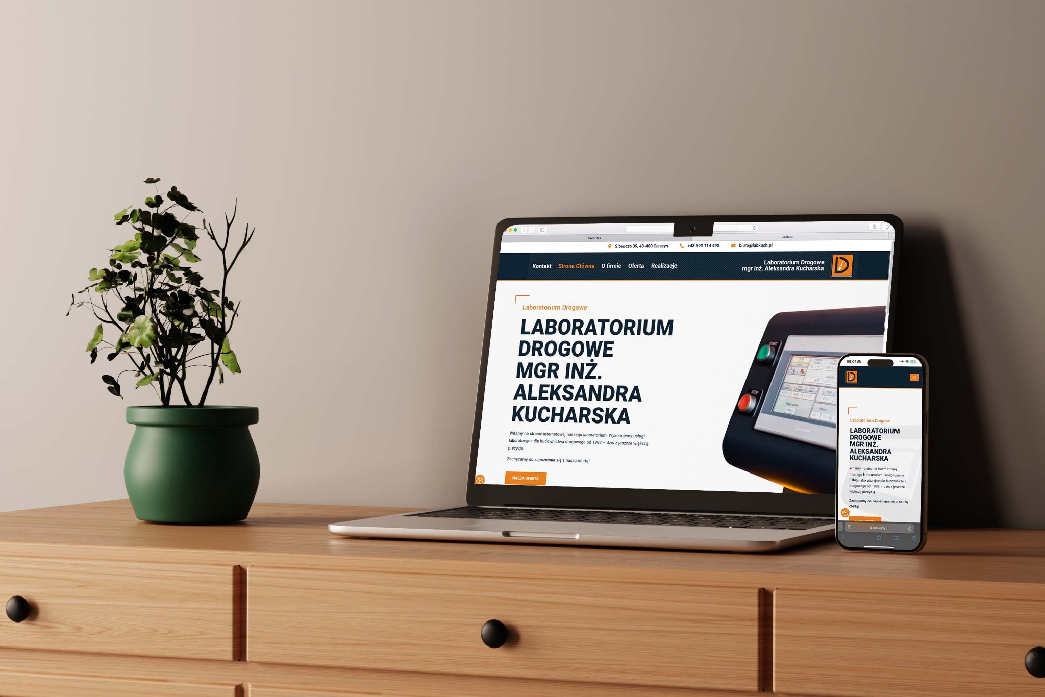 Responsywna strona www na laptopie i smartfonie, prezentująca ofertę laboratorium drogowego, z rośliną doniczkową obok, na drewnianej komodzie z szufladami.