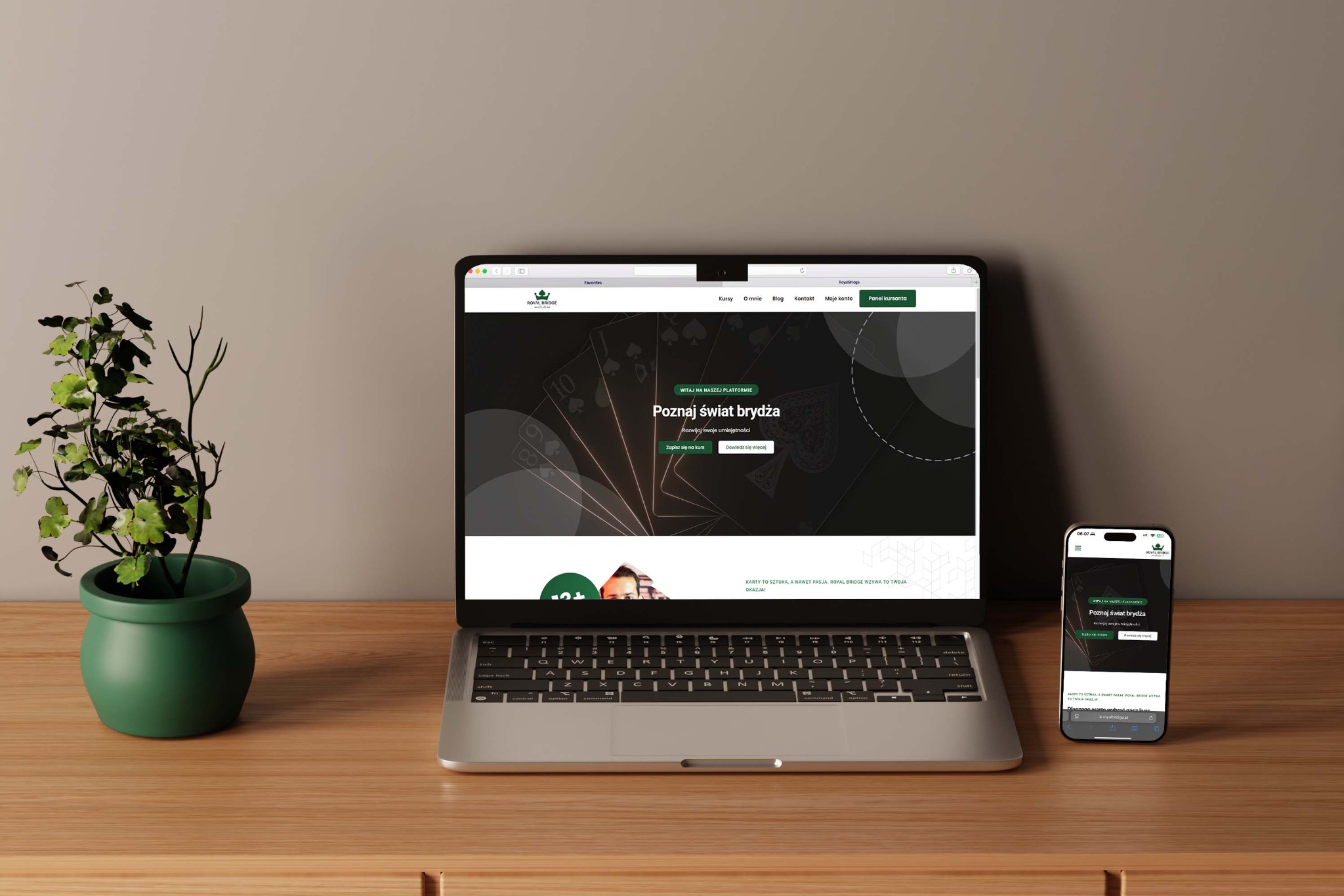 Laptop i smartfon prezentują stronę o brydżu 'Royal Bridge' na drewnianym biurku obok rośliny doniczkowej. Ekran laptopa w centrum uwagi.