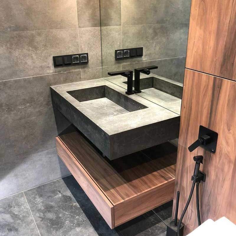 Nowoczesna łazienka z szarą, kamienną umywalką o geometrycznym kształcie, czarną armaturą i drewnianą szafką pod umywalką, uzupełniona o bidetkę w tym samym kolorze.