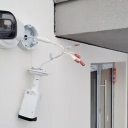 Montaż kamery monitoringu Dahua na elewacji budynku, widoczne kable z końcówkami do podłączenia, uchwyt kamery i korpus kamery z naklejką informacyjną.