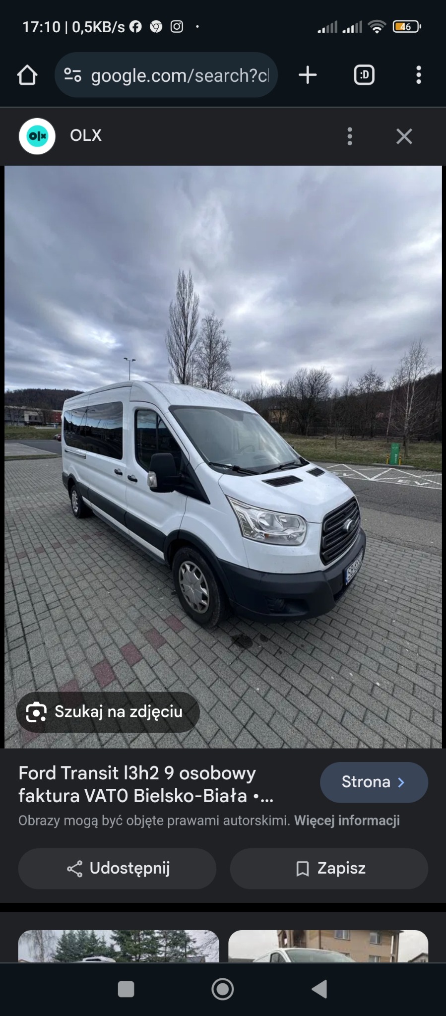 Biały bus Ford Transit L3H2, zaparkowany na brukowanej powierzchni, widok z przodu pod kątem, pochmurne niebo w tle.