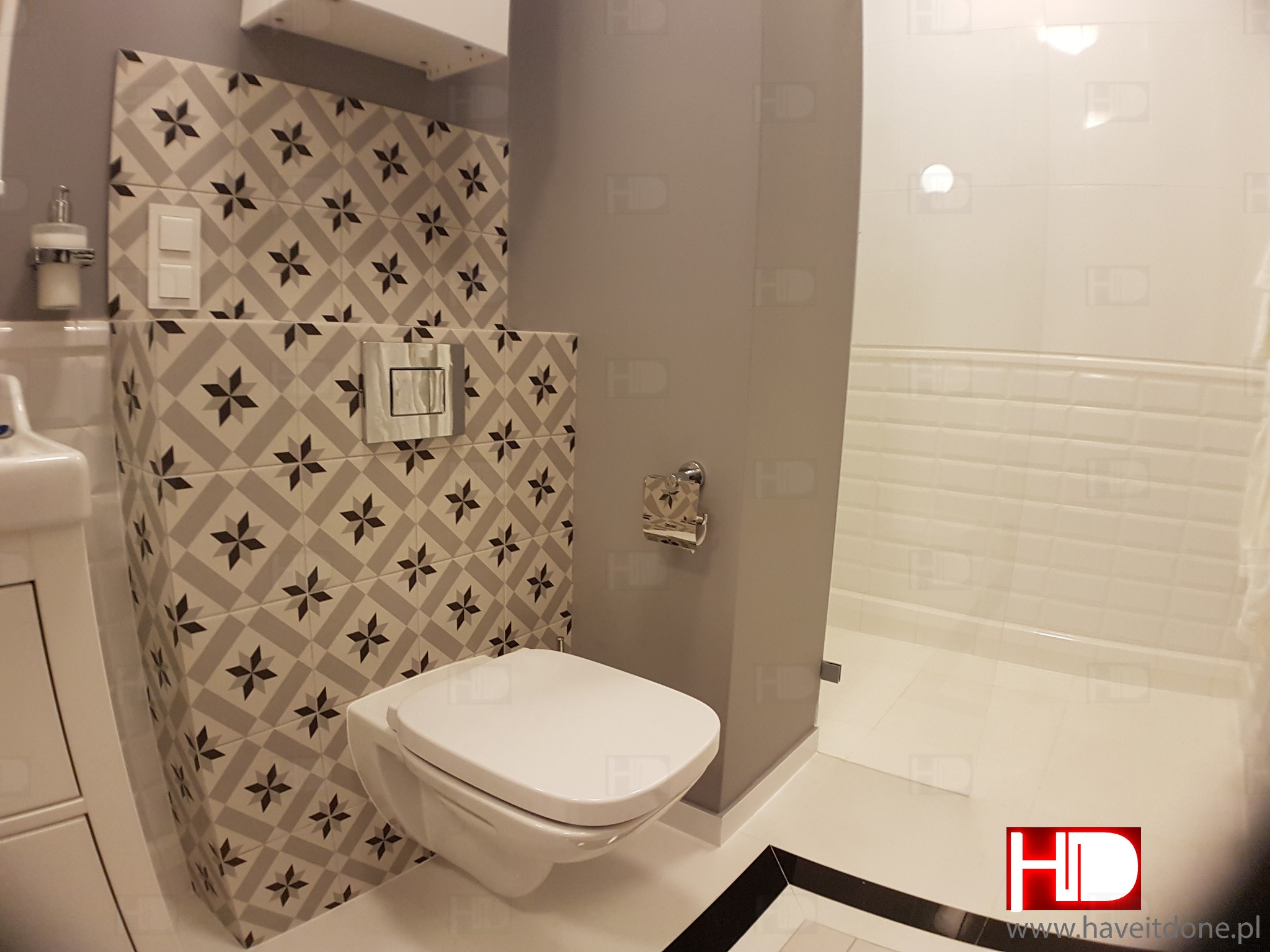 Wnętrze łazienki z wiszącą toaletą, płytkami w geometryczny wzór i minimalistycznym wyposażeniem.