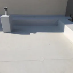 Płaski dach pokryty białą membraną, widoczny komin wentylacyjny oraz obróbki blacharskie przy krawędziach dachu.