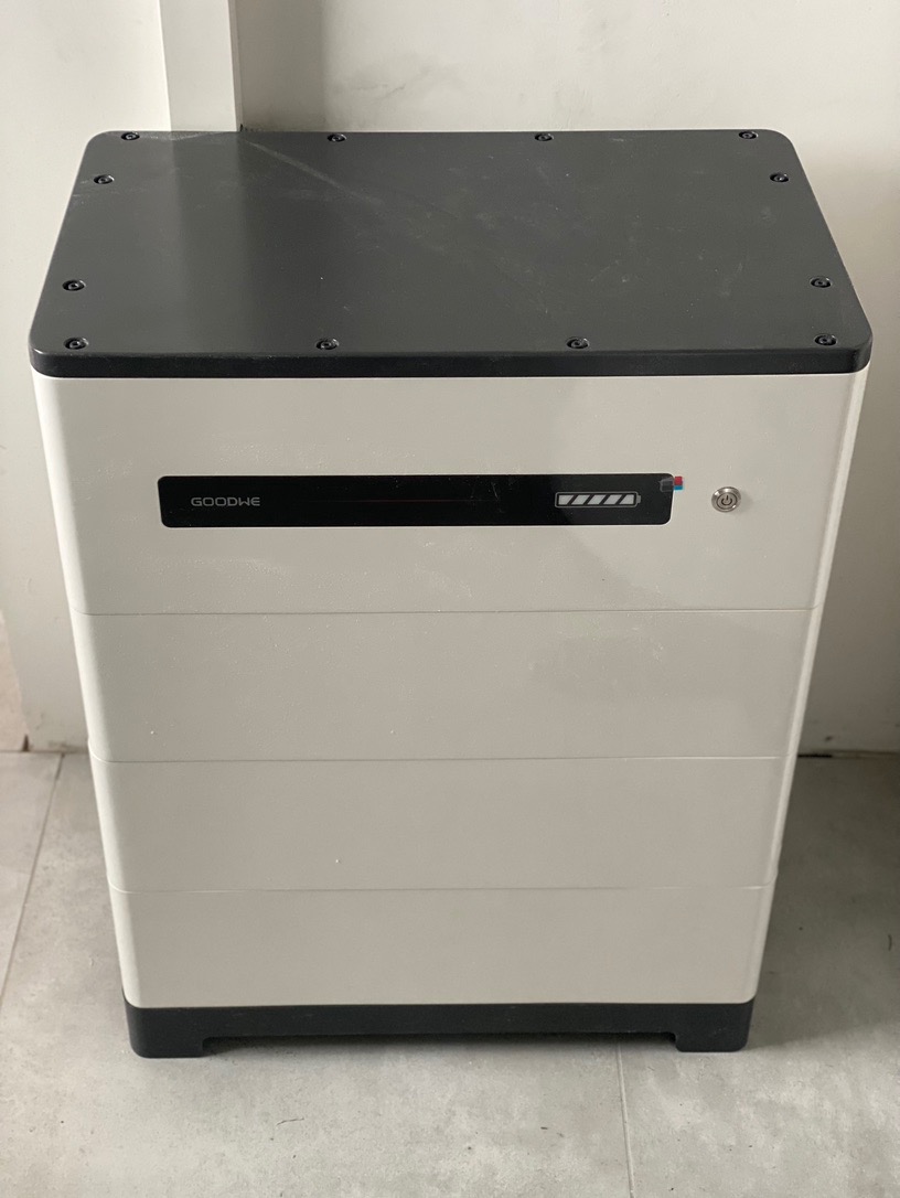 Biało-czarny magazyn energii GoodWe z widocznym wskaźnikiem naładowania umieszczony w rogu pomieszczenia.