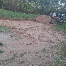 KARO SPÓŁKA Z OGRANICZONĄ ODPOWIEDZIALNOŚCIĄ - Teren wyrównany koparką, przygotowany pod budowę, z widocznym stosem ziemi i oznaczeniami geodezyjnymi.