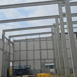 KamBud - Wnętrze budowanej hali z betonu komórkowego i prefabrykatów, widoczny podnośnik koszowy i elementy konstrukcyjne. Surowy stan, etap budowy.