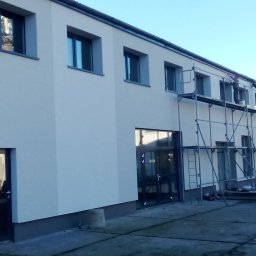 MatSolid-Bud - Budynek po renowacji elewacji, z rusztowaniami i pracownikami podczas malowania. Widoczne okna i drzwi, świeża, jasna elewacja.