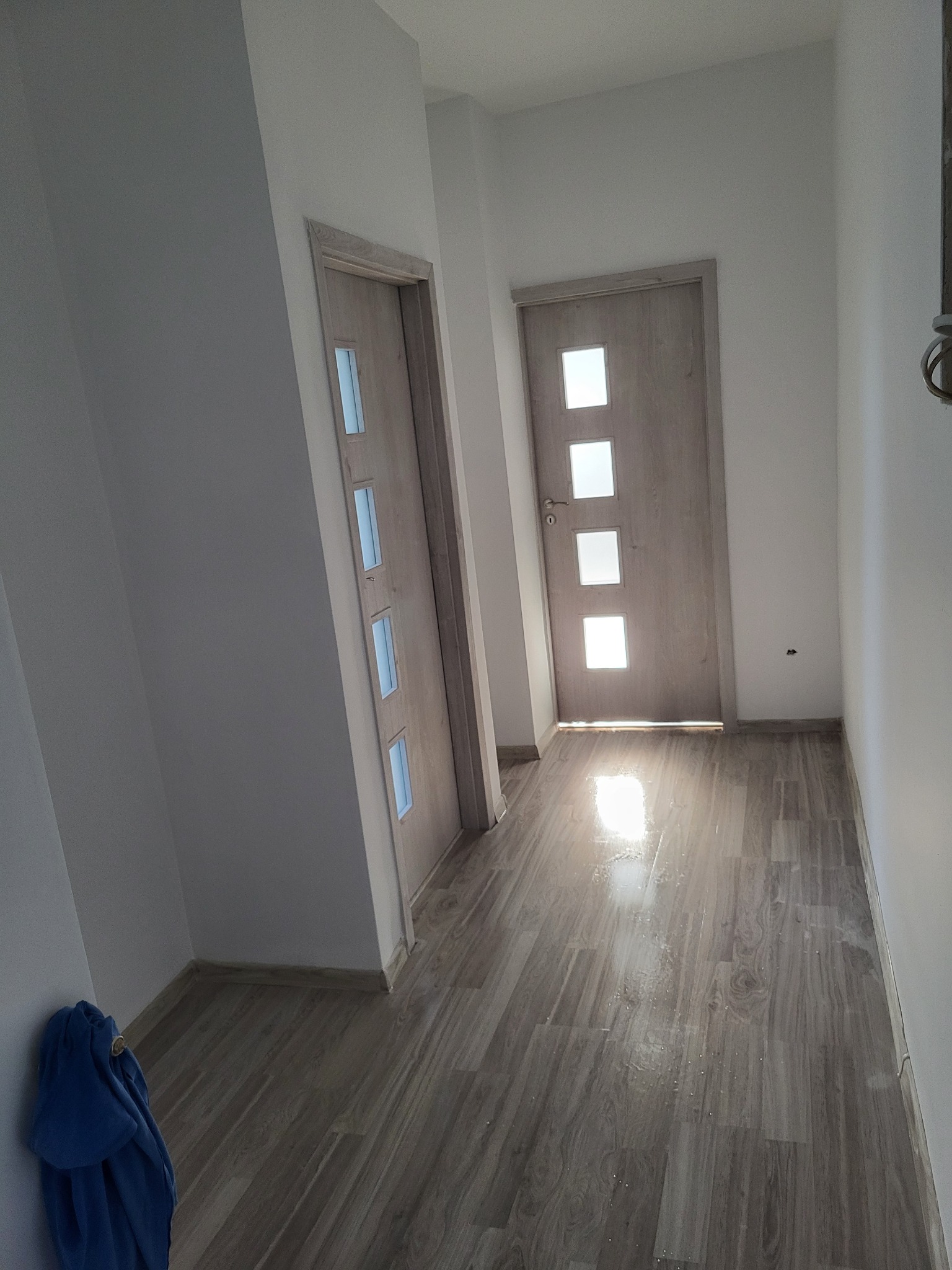 Wnętrze po remoncie: jasne ściany, drewnopodobne panele, dwie drewniane drzwi z przeszkleniami, fragment niebieskiego materiału w rogu.