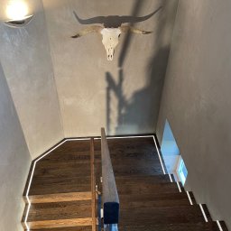 R S Budownictwo - Klatka schodowa z drewnianymi stopniami oświetlonymi listwami LED, ściana wykończona w stylu betonu architektonicznego, dekoracja w postaci czaszki byka z rogami na ścianie.