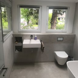 R S Budownictwo - Nowoczesna łazienka w szarościach z wiszącą umywalką, toaletą i wanną, z widokiem na zieleń za oknem