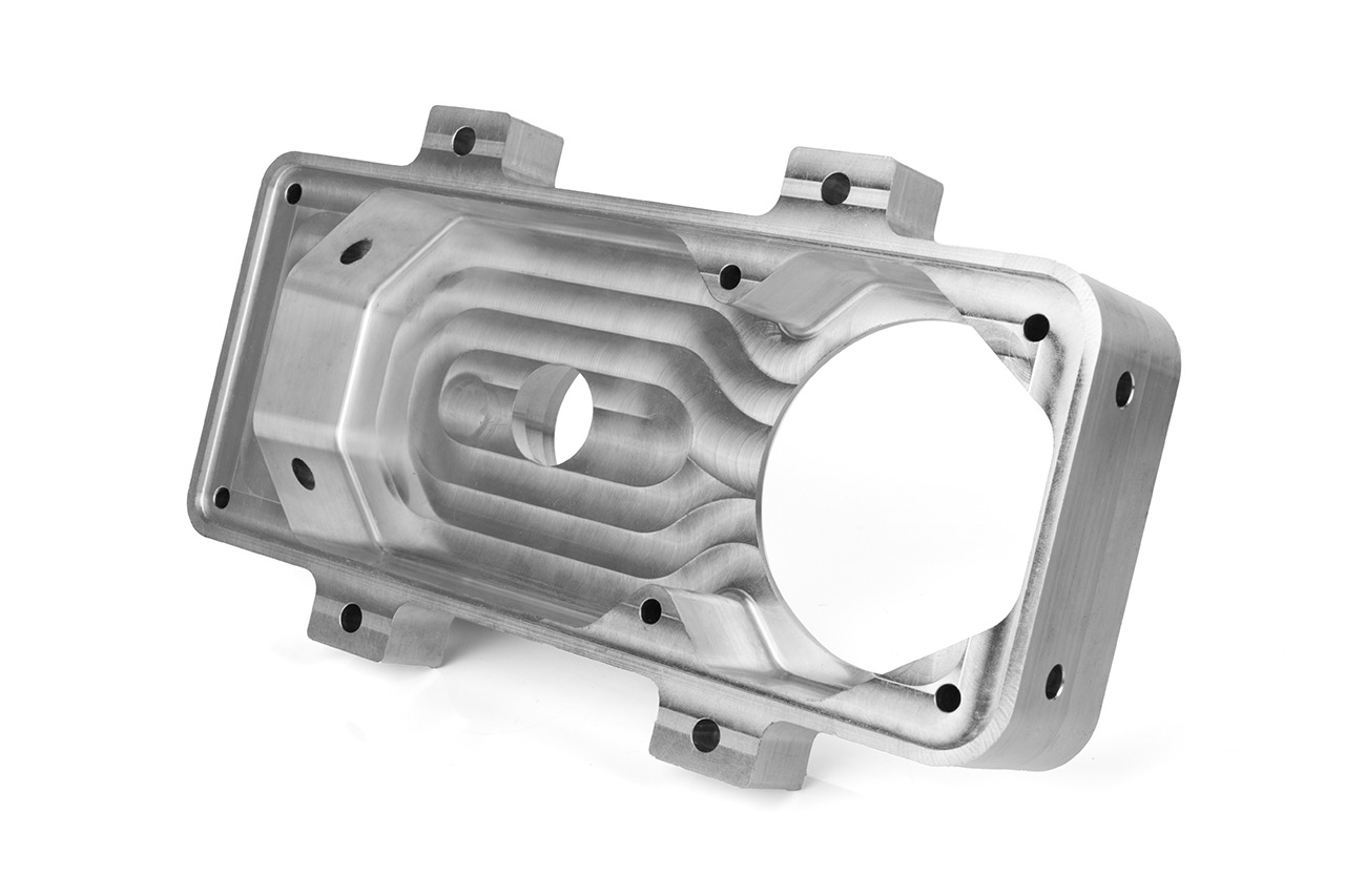 Precyzyjnie obrobiony, aluminiowy element z widocznymi śladami frezowania i otworami montażowymi, leżący na białym tle.