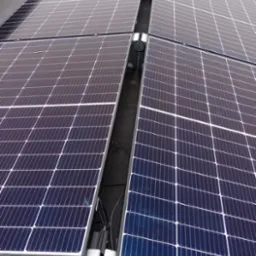 Rząd paneli słonecznych z widocznymi elementami montażowymi i okablowaniem na płaskim dachu.